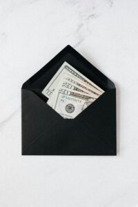 Top view of opened envelope with USA banknotes of 20 dollars placed on white marble desk illustrating concept of money gift or charity