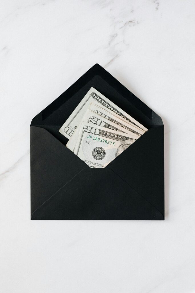 Top view of opened envelope with USA banknotes of 20 dollars placed on white marble desk illustrating concept of money gift or charity
